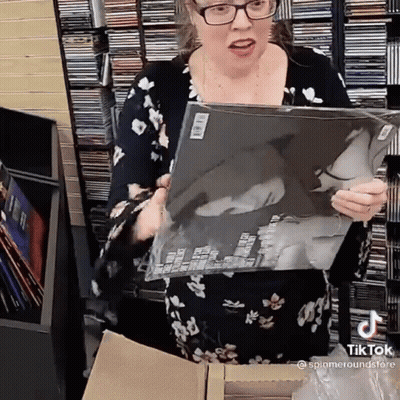 Woman In Floral Dress Holding Record In Front Of CD Shelf GIF