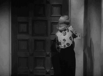Woman In Floral Shirt Standing At Door In Black And White Photo GIF