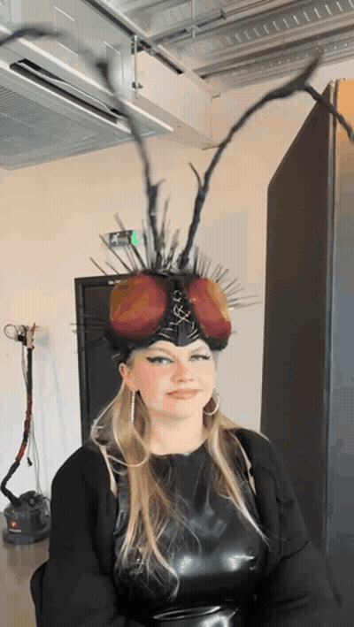 Woman In Fly Headpiece With Green Exit Sign GIF