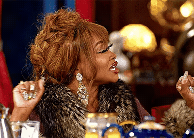 Woman In Fur Vest With Hands In Air At Table GIF