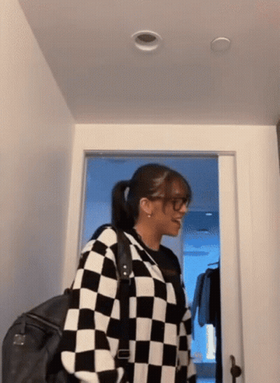 Woman In Glasses And Checkered Sweater Standing In Hallway GIF