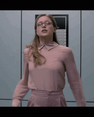 Woman In Glasses And Pink Shirt Standing Before Sign Saying A GIF