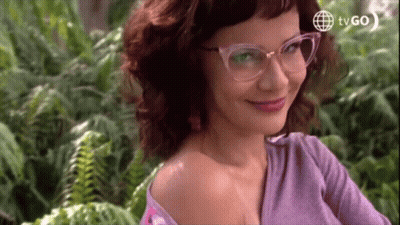 Woman In Glasses And Purple Shirt Smiling In Front Of Ferns And TVGO Logo GIF