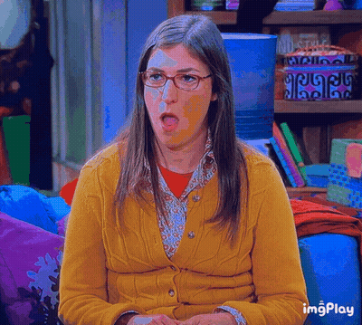 Woman In Glasses And Yellow Cardigan Sitting On Couch With Mouth Open GIF