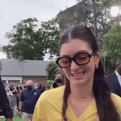 Woman In Glasses And Yellow Shirt Smiling At Crowd GIF