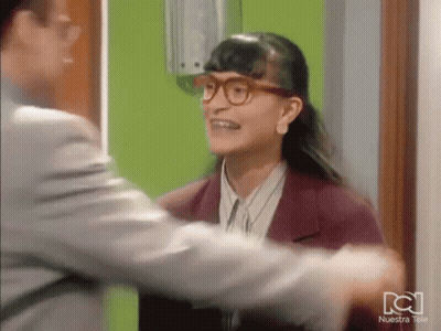 Woman In Glasses Hugging Man In Front Of Nuestra Tele Green Wall GIF
