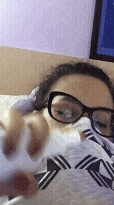 Woman In Glasses Laying On Bed With Tissue In Mouth GIF