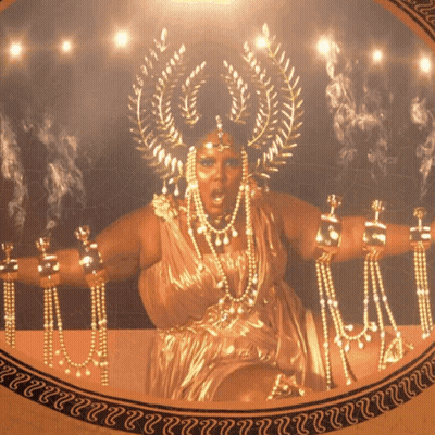 Woman In Gold Dress With Crown Surrounded By Gold Jewelry GIF