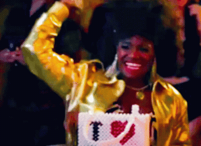 Woman In Gold Jacket Holding Purse Saying I Love You GIF