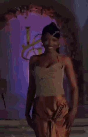 Woman In Gold Top And Orange Skirt In Front Of Purple Archway GIF