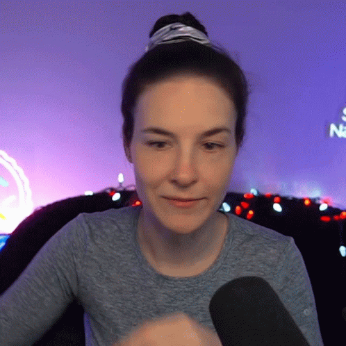 Woman In Gray Shirt Sitting In Front Of Neon Sign Saying Na GIF