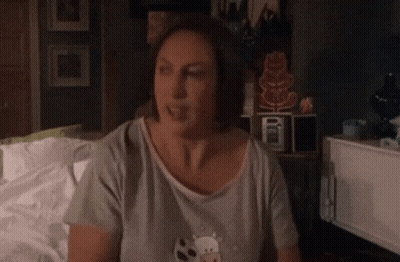Woman In Gray Shirt Sitting On Bed GIF