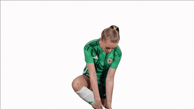 Woman In Green Adidas Shirt Holding Shoe To Ear GIF