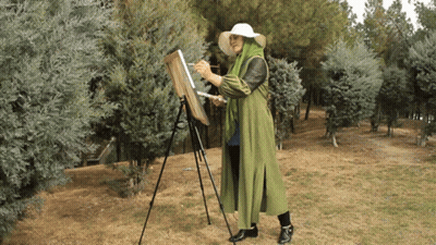 Woman In Green Coat Painting On Easel In Woods GIF