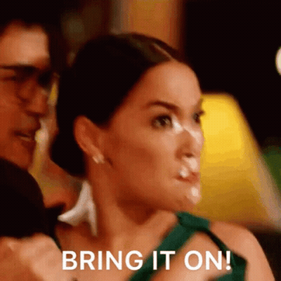 Woman In Green Dress Holding Man's Arm Says Bring It On GIF