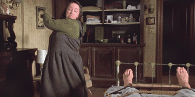 Woman In Green Dress Holding Stick Over Man On Bed GIF