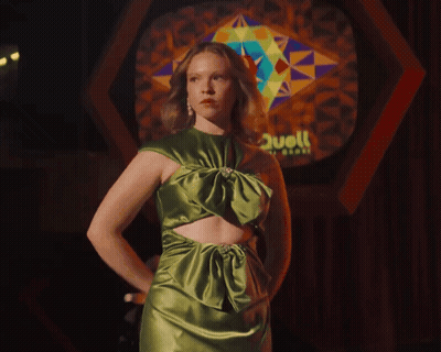 Woman In Green Dress Holding Sticks In Front Of Stained Glass Saying Hell GIF