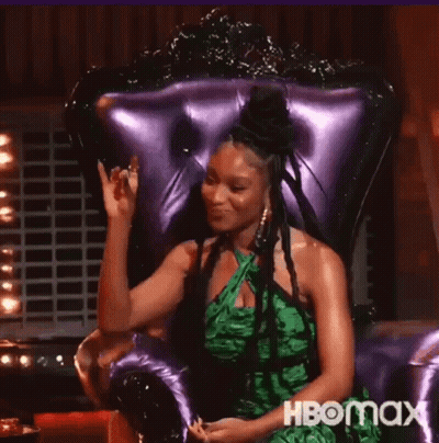 Woman In Green Dress Waving In Purple Chair GIF