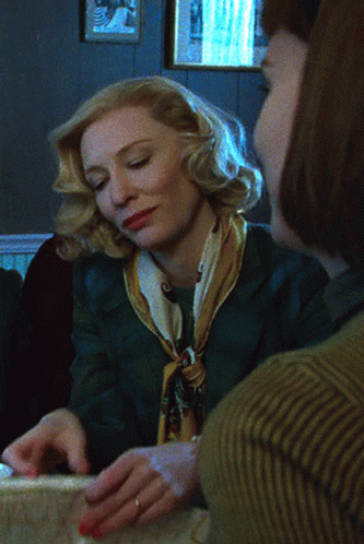 Woman In Green Jacket And Yellow Scarf Sitting With Another Woman GIF