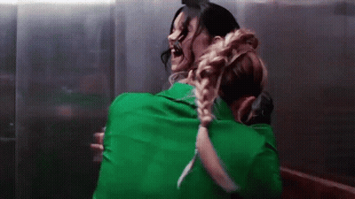 Woman In Green Shirt Hugging Another Woman In Dark Room GIF