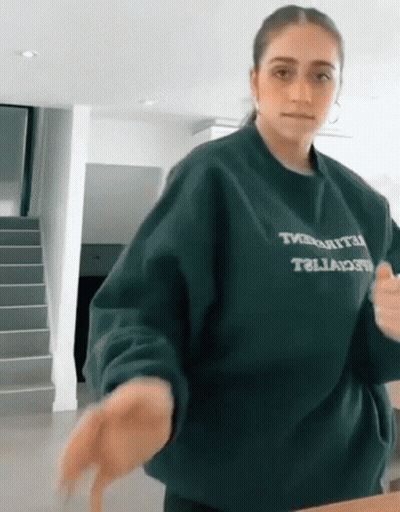 Woman In Green Sweater Saying Tivoli Standing In Front Of Stairs GIF
