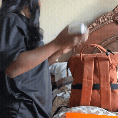 Woman In Grey Shirt Holding Bottle Beside Orange Backpack GIF