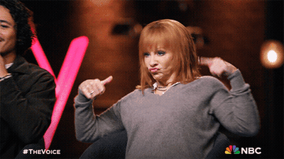 Woman In Grey Sweater Making Funny Face In Front Of NBC Sign GIF