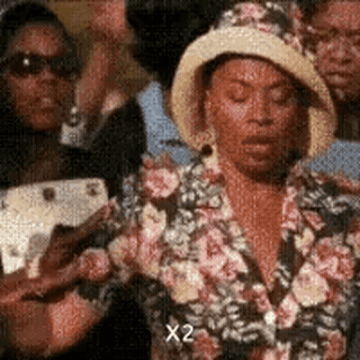 Woman In Hat And Floral Jacket Standing In Crowd GIF