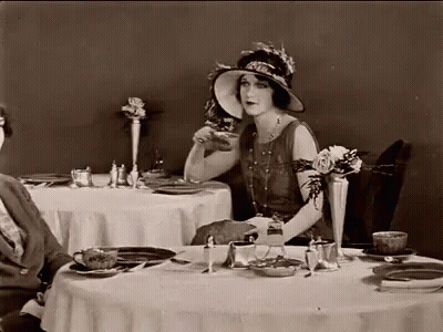 Woman In Hat Sitting At Table With Plates And Cups GIF
