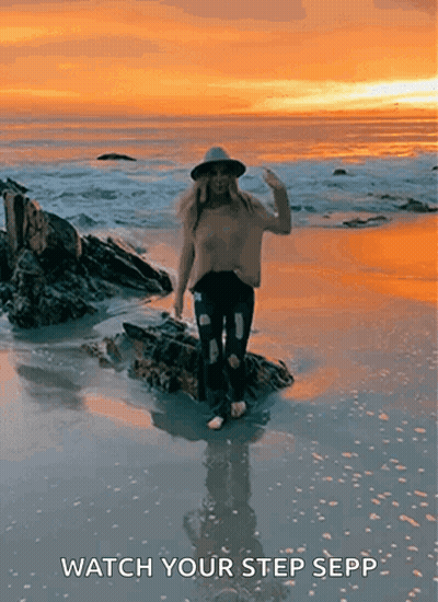 Woman In Hat Standing On Rock At Sunset GIF