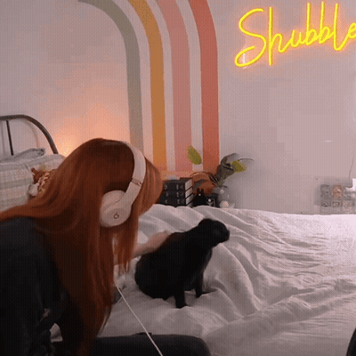 Woman In Headphones On Bed With Shubble Neon Sign GIF