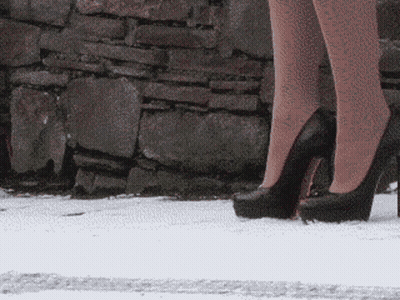 Woman In High Heels Standing In Snow In Front Of Stone Wall GIF