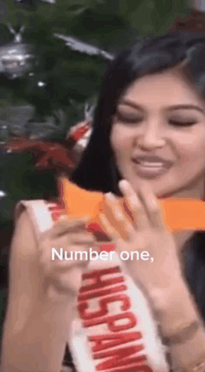Woman In Hispanic Sash Holding Paper In Front Of Christmas Tree GIF