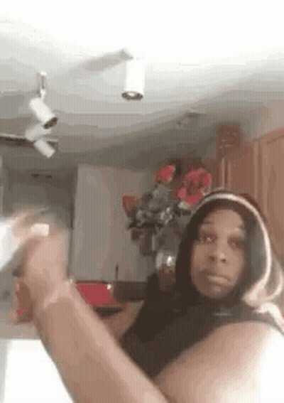 Woman In Hoodie Taking Selfie In Kitchen With Flowers GIF