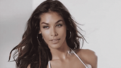 Woman In Hoop Earrings And White Bikini Top Looking At Camera GIF