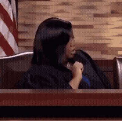 Woman In Judge Robe Sitting At Table In Front Of American Flag GIF