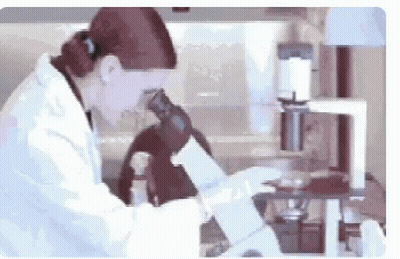 Woman in Lab Coat Looking Through Microscope