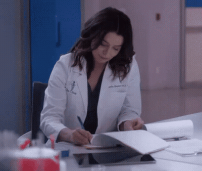 Woman In Lab Coat Writing In Notebook At Desk GIF