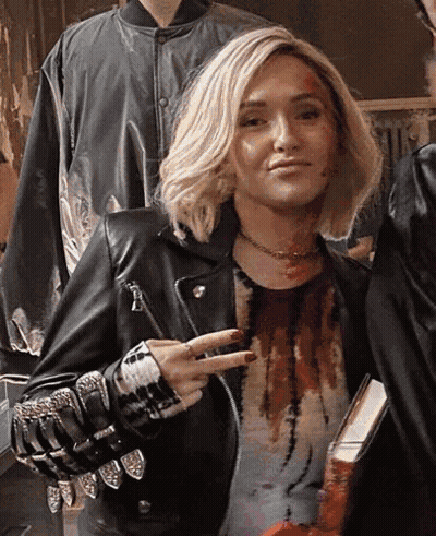 Woman In Leather Jacket Giving Peace Sign Holding Book GIF