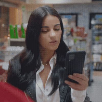 Woman In Leather Jacket Looking At Phone In Store GIF