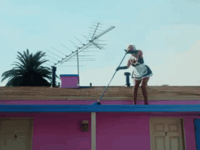 Woman In Maid Outfit Holding Mop On Pink Building Roof GIF