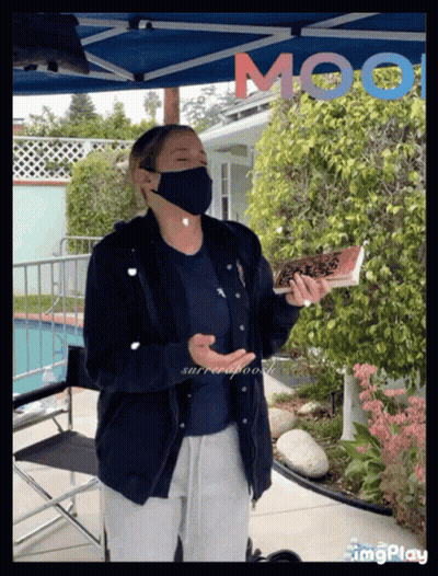 Woman In Mask Holding Book In Front Of Moot Sign GIF