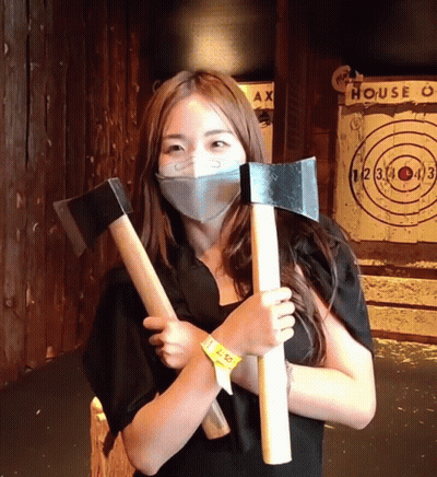 Woman In Mask Holding Two Axes With House Target GIF