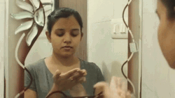 Woman In Mirror Rubbing Lotion On Face GIF