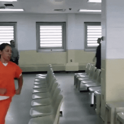 Woman In Orange Scrubs Running Through Chairs GIF