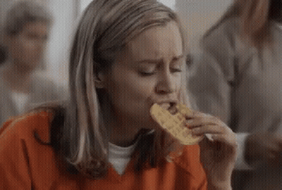 Woman In Orange Shirt Eating Waffle In Jail Cell GIF