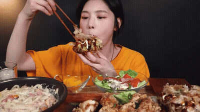 Woman In Orange Shirt Eating With Chopsticks GIF