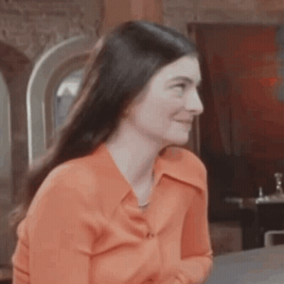 Woman In Orange Shirt Sitting GIF
