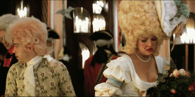 Woman In Pearl Necklace Next To Man In Costume GIF
