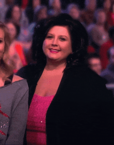 Woman In Pink Dress And Black Jacket Smiling Before Crowd GIF